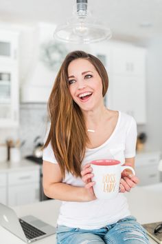 a woman sitting on a kitchen counter holding a coffee mug with the words boss lady printed on it