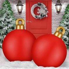 two red christmas balls sitting in front of a red door with wreath on the top