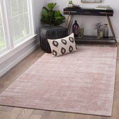 a pink rug with black and white designs on it in front of a window next to a plant