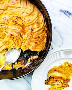 a pan filled with food sitting on top of a white counter next to plates and utensils