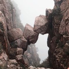 a person standing on the side of a mountain looking up at an arch in the rock