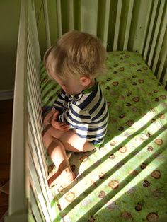 a little boy sitting in his crib looking at something on the ground below him