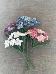 crocheted flowers are arranged on a gray surface with white, pink, blue and green stems