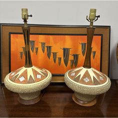 two decorative vases sitting on top of a wooden table next to a framed painting