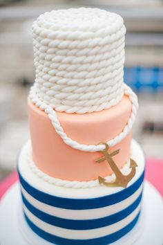 a three tiered cake with an anchor and rope on the top, sitting on a table