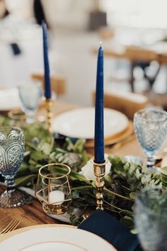 the table is set with blue candles and greenery for an elegant touch to the place setting