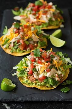 three tortillas topped with chicken, lettuce and tomatoes on a black tray