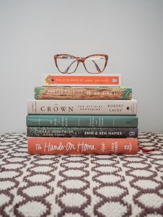 a stack of books sitting on top of a bed next to a pair of glasses