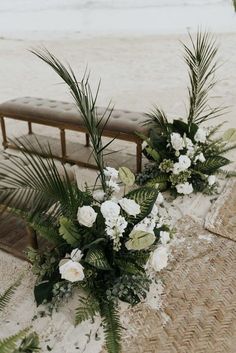 flowers and greenery are arranged on a bench by the beach