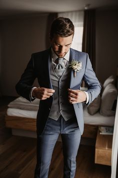 a man in a suit and bow tie is looking at his cell phone while standing next to a bed