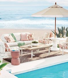 an outdoor living area next to a pool and beach with chairs, tables and umbrellas