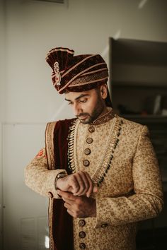 a man in a turban looking at his cell phone while wearing a red and gold outfit