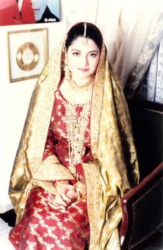 a woman in a red and gold dress sitting on a chair with her hands clasped