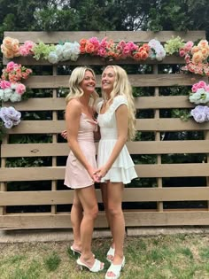 two beautiful young women standing next to each other in front of a flower covered wall