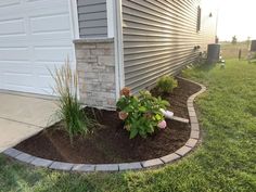 a flower bed in front of a house with flowers growing out of the mulch