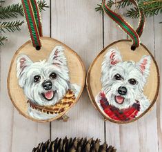 two wooden ornaments with white dogs painted on them and pine cones next to each other