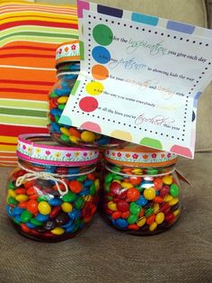 three jars filled with colorful candy sitting on top of a couch next to a pillow