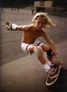 a shirtless boy riding a skateboard on top of a basketball court with his leg in the air