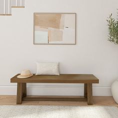 a wooden bench sitting in front of a white wall with a hat on top of it