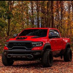 a red ram truck parked in the middle of a forest with lots of leaves on the ground