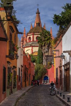 a motorcycle parked in the middle of an alley way with buildings on both sides and palm trees