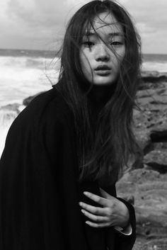 a woman with long hair standing by the ocean