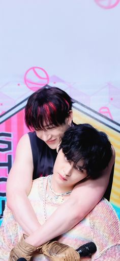 two young men hugging each other while sitting on top of a bean bag chair in front of a colorful wall