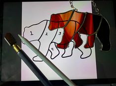 a stained glass bear is hanging from a chain next to a paintbrush and pen