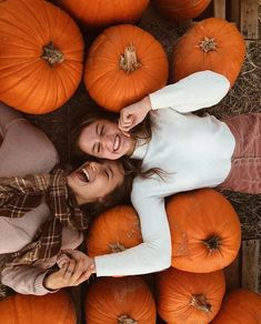 two women standing next to each other surrounded by pumpkins