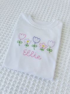 a white t - shirt with flowers embroidered on the front that says,'elsie '