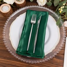 a table setting with green napkins, silverware and white flowers on the side