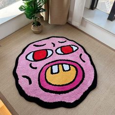 a pink rug with an angry face on the floor in front of a potted plant