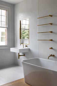 a white bath tub sitting under a window next to a sink in a bathroom with gold faucets