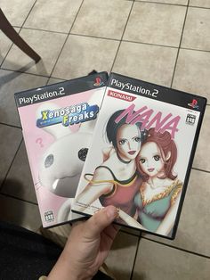 two video game covers being held up in front of a person's hand on the floor