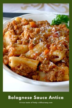 a white bowl filled with pasta and meat on top of a table next to a fork