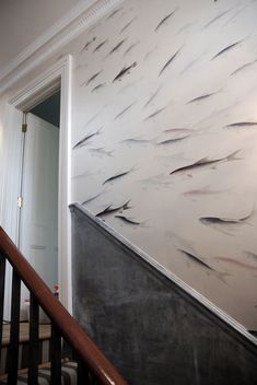 a wall with fish painted on it next to a stair case in a room that has white walls and wood handrails