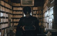 a person standing in front of a bookshelf holding an electronic device and looking at it