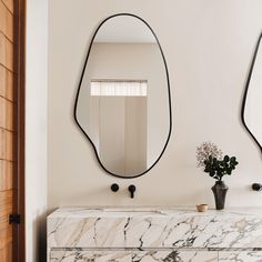 two mirrors are on the wall above a marble counter top and a vase with flowers in it