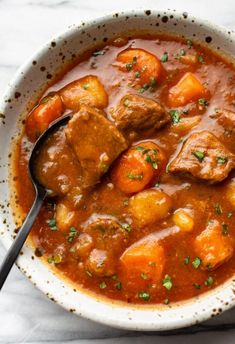 a white bowl filled with stew and carrots on top of a marble countertop