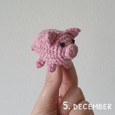 a small pink crocheted pig sitting on top of someone's finger in front of a white wall