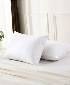 two white pillows sitting on top of a bed next to a potted green plant