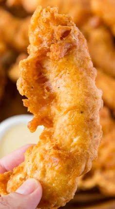 a person holding up a fried chicken nugget with ranch dressing in the background