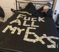 a man laying on top of a bed covered in money and fake words that spell out the word