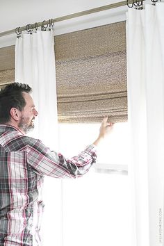 a man standing in front of a window with his hand on the curtain valance