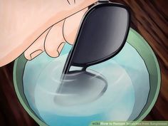 a hand holding a pair of sunglasses over a bowl of blue liquid with water in it