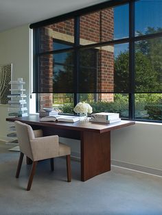 a desk with books and flowers on it in front of a window that looks out onto the street