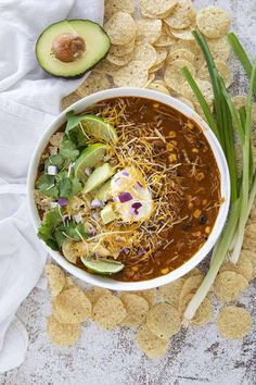 a white bowl filled with chili and tortilla chips next to an avocado