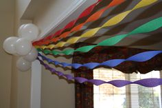 balloons and streamers hang from the ceiling in front of a window decorated with multicolored ribbons