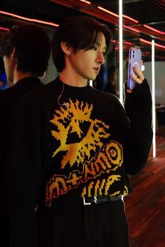 a person holding a cell phone and wearing a sweater with an image of a dragon on it