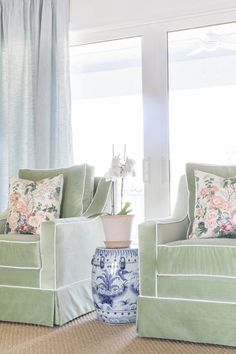 a living room with two green chairs and a blue vase in front of the window